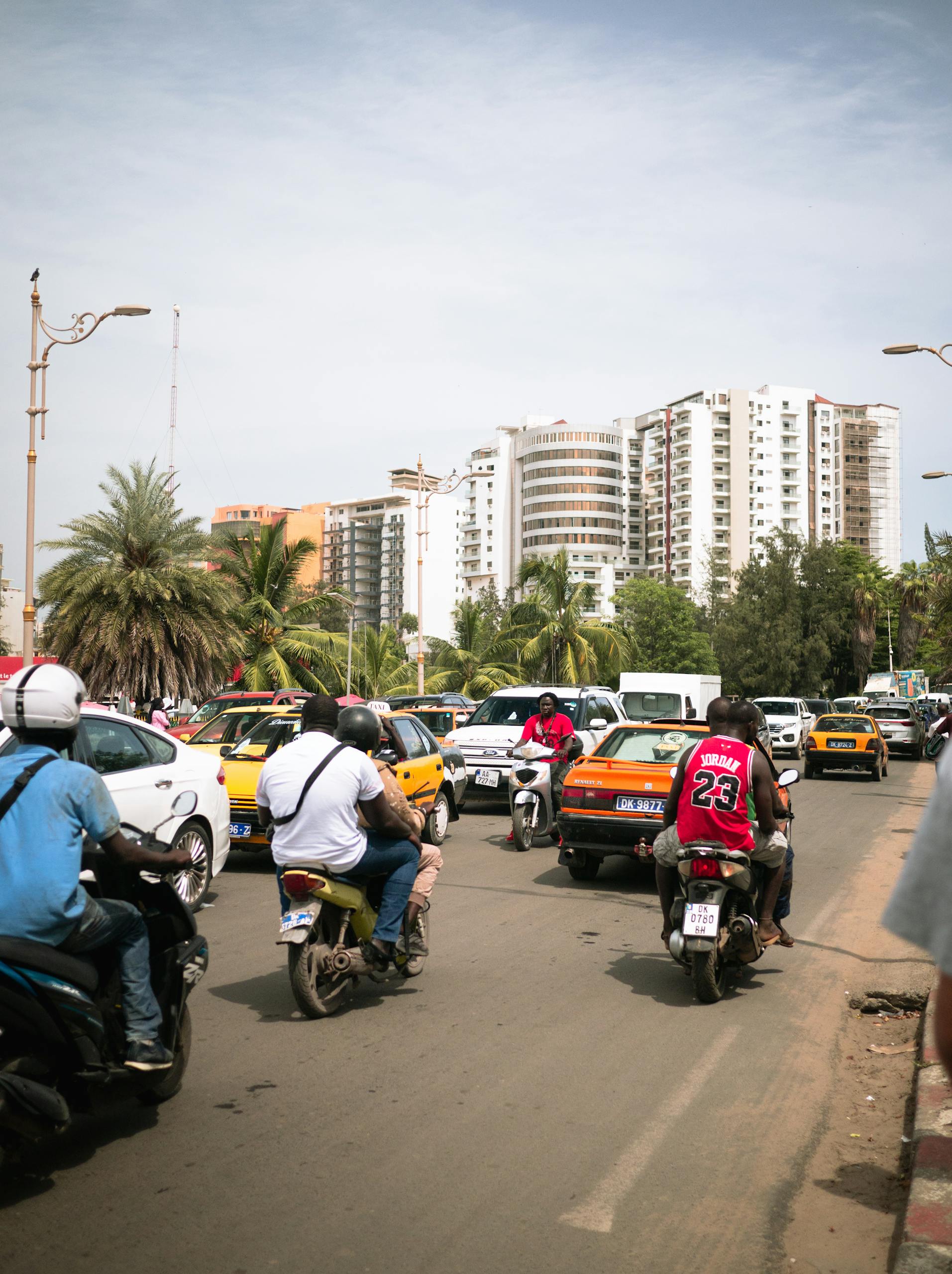 City street in Dakar with motorbikes and cars navigating heavy traffic, showcasing urban life.